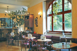 Das Museumscafé ist eingerichtet mit Jugendstilmöbeln, braune Holzstühle, runde Tische mit Marmorplatte und Lampenschirme in Blütenkelchform machen die Atmosphäre gemütlich.
